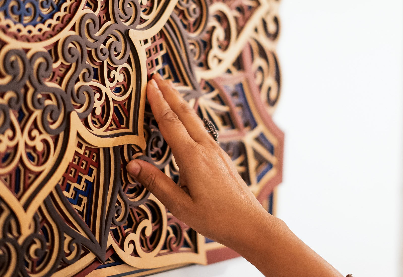 Hand touching a detailed wooden wall art piece with intricate patterns.
